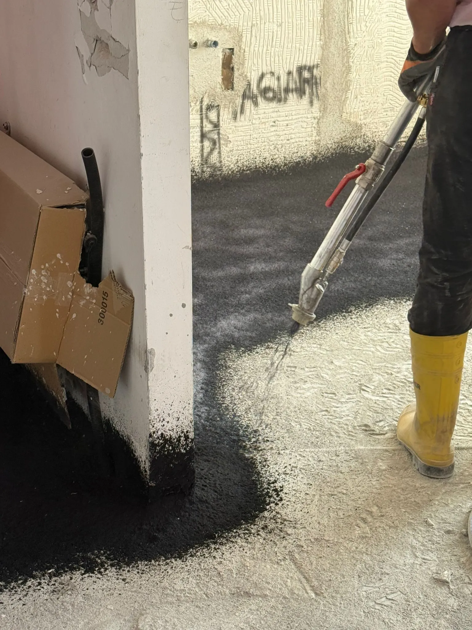 Applicazione a spruzzo della gomma acustica Isospray lungo una parete, attorno a una tubazione